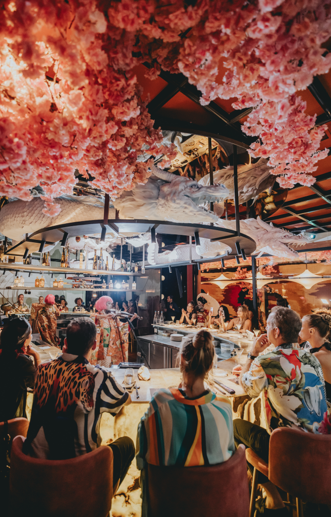 Comensales disfrutando de la noche Sakuran en Miss Fish bajo un techo de flores de cerezo rosa y esculturas de dragón.